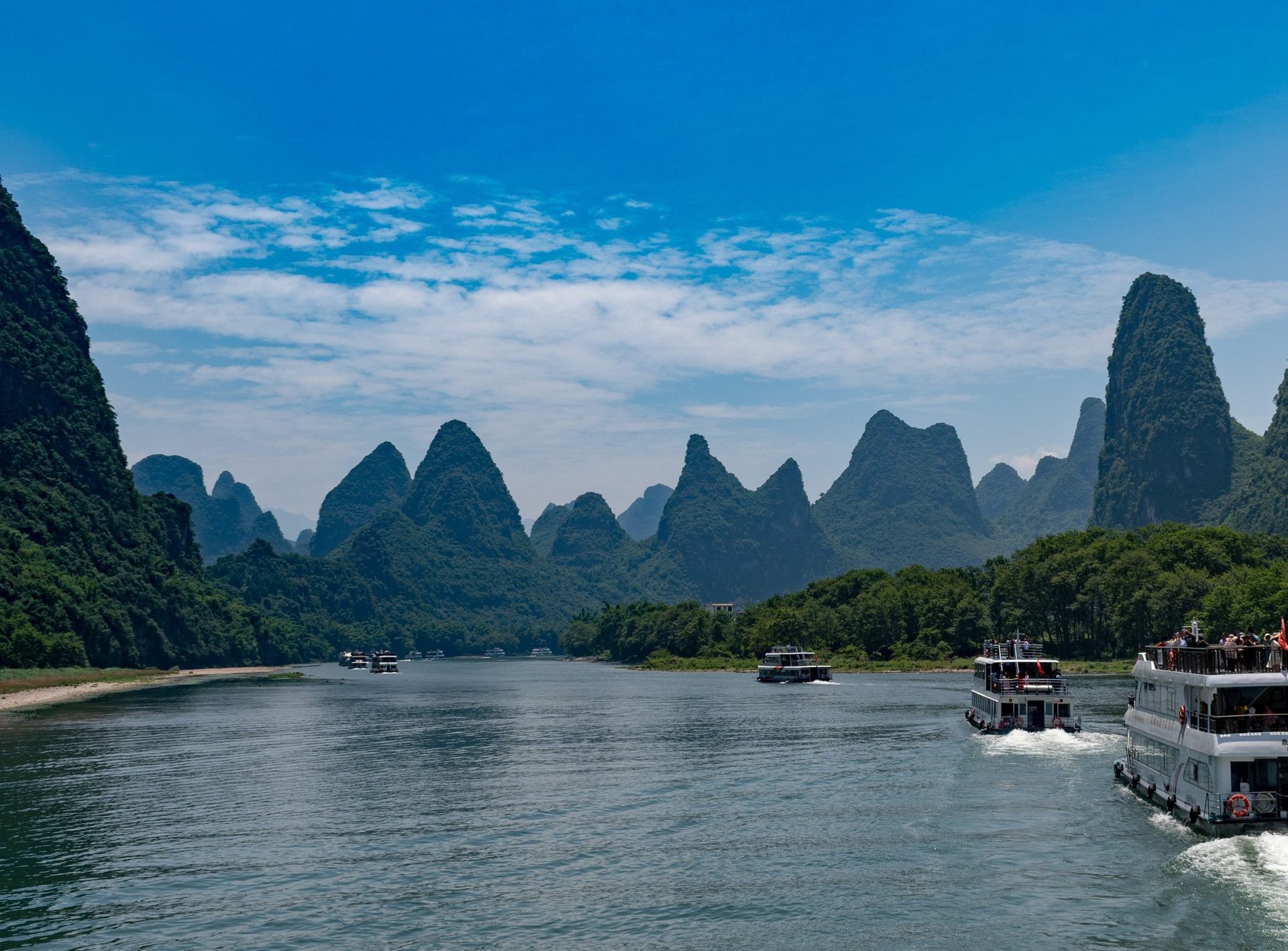 Karst limestone peaks lining the Li River near Guilin with tour boats on the water — Photo: xiquinhosilva / CC BY 2.0 via Wikimedia Commons