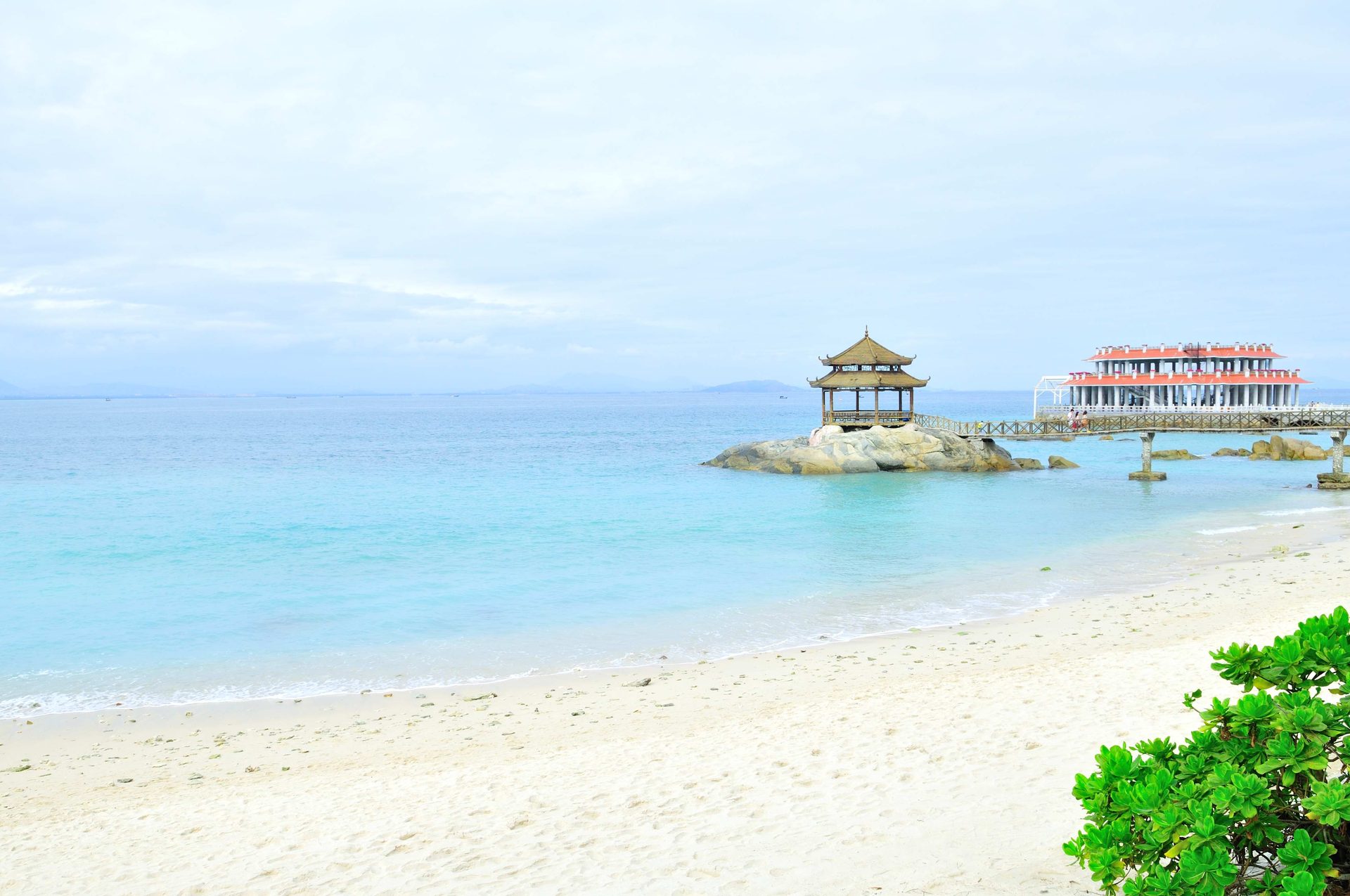 White sand beach and turquoise water at Wuzhizhou Island, Sanya, Hainan, with a Chinese pavilion on the rocks